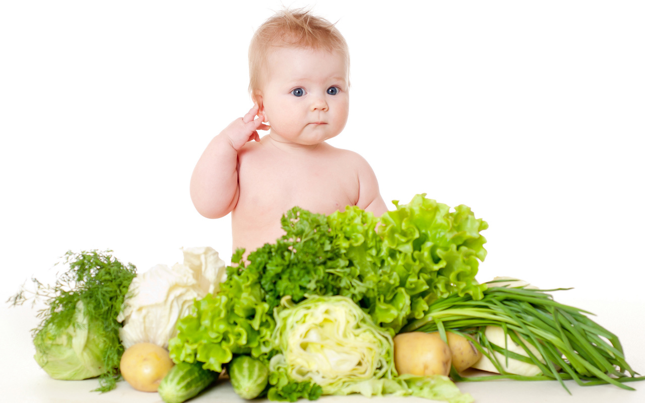 Маленький ребенок с овощами и зеленью на белом фоне