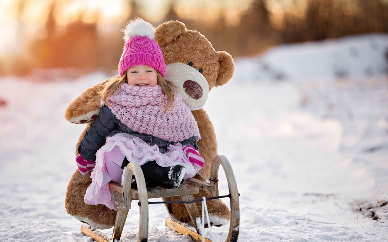 Маленькая девочка на санках с большим медведем зимой 