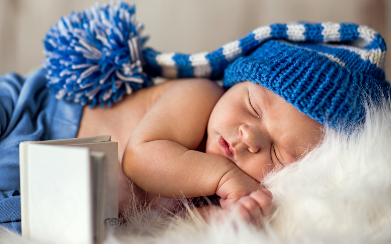 Маленький спящий грудной ребенок в синей вязанной шапке 