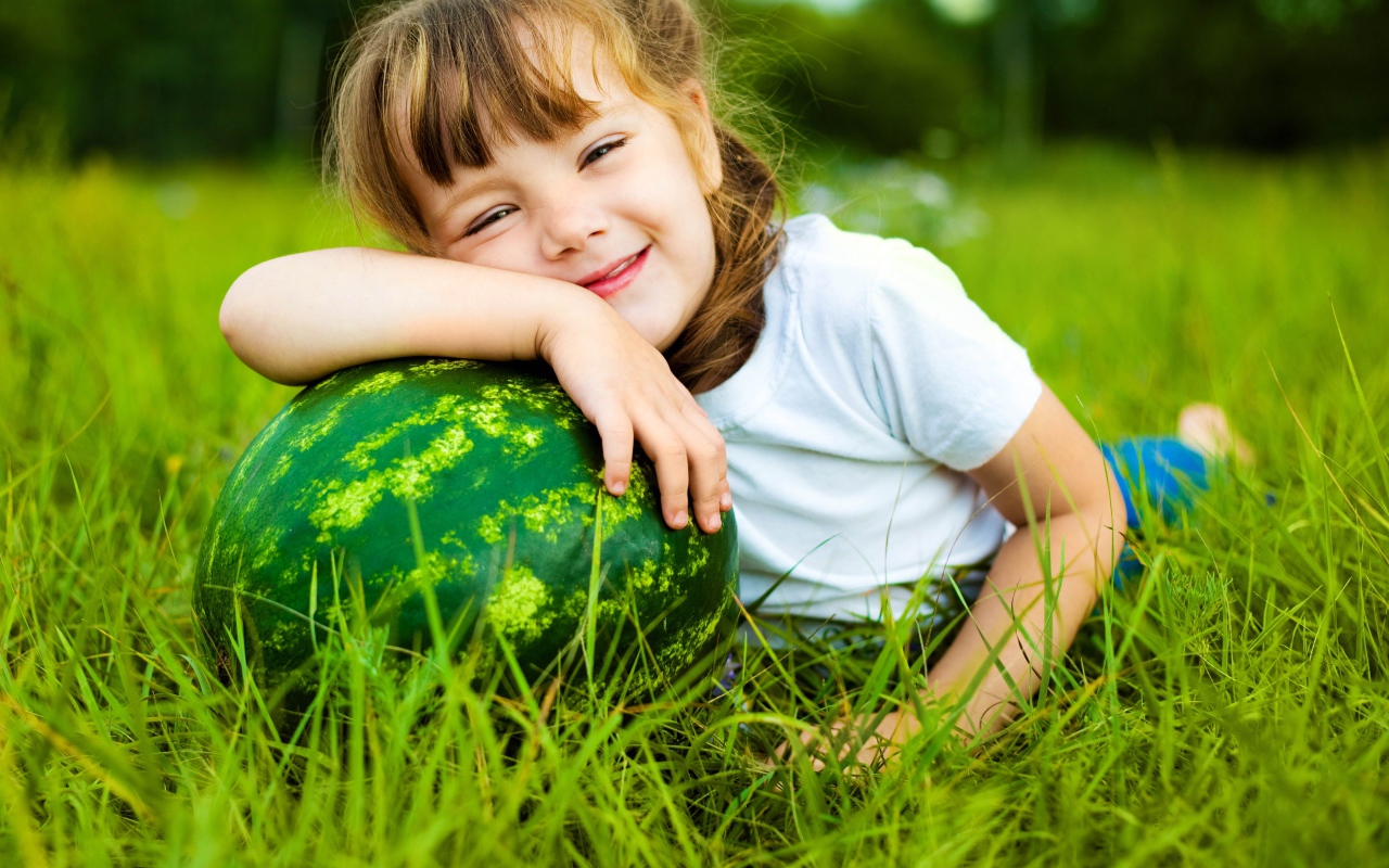 Улыбающаяся девочка с зеленым арбузом на траве