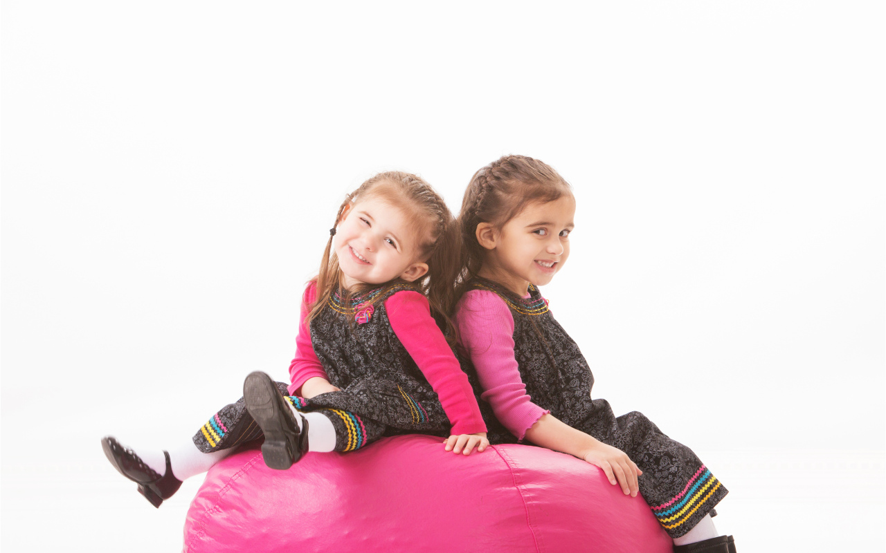 Две маленькие девочки сидят на красном мягком шаре 