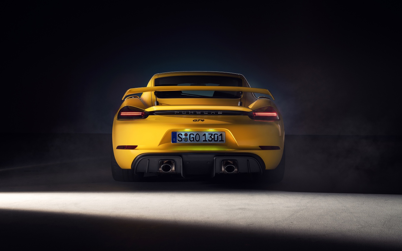 Желтый автомобиль Porsche 718 Cayman GT4, 2019 года вид сзади на сером фоне