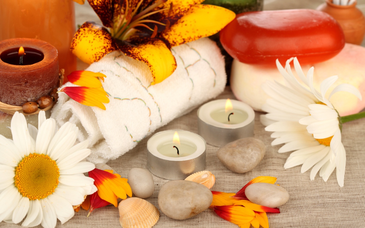 Зажженные свечи на столе с полотенцем, цветами и мылом