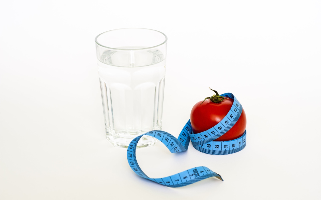 Стакан воды на белом фоне с красным помидором и сантиметром