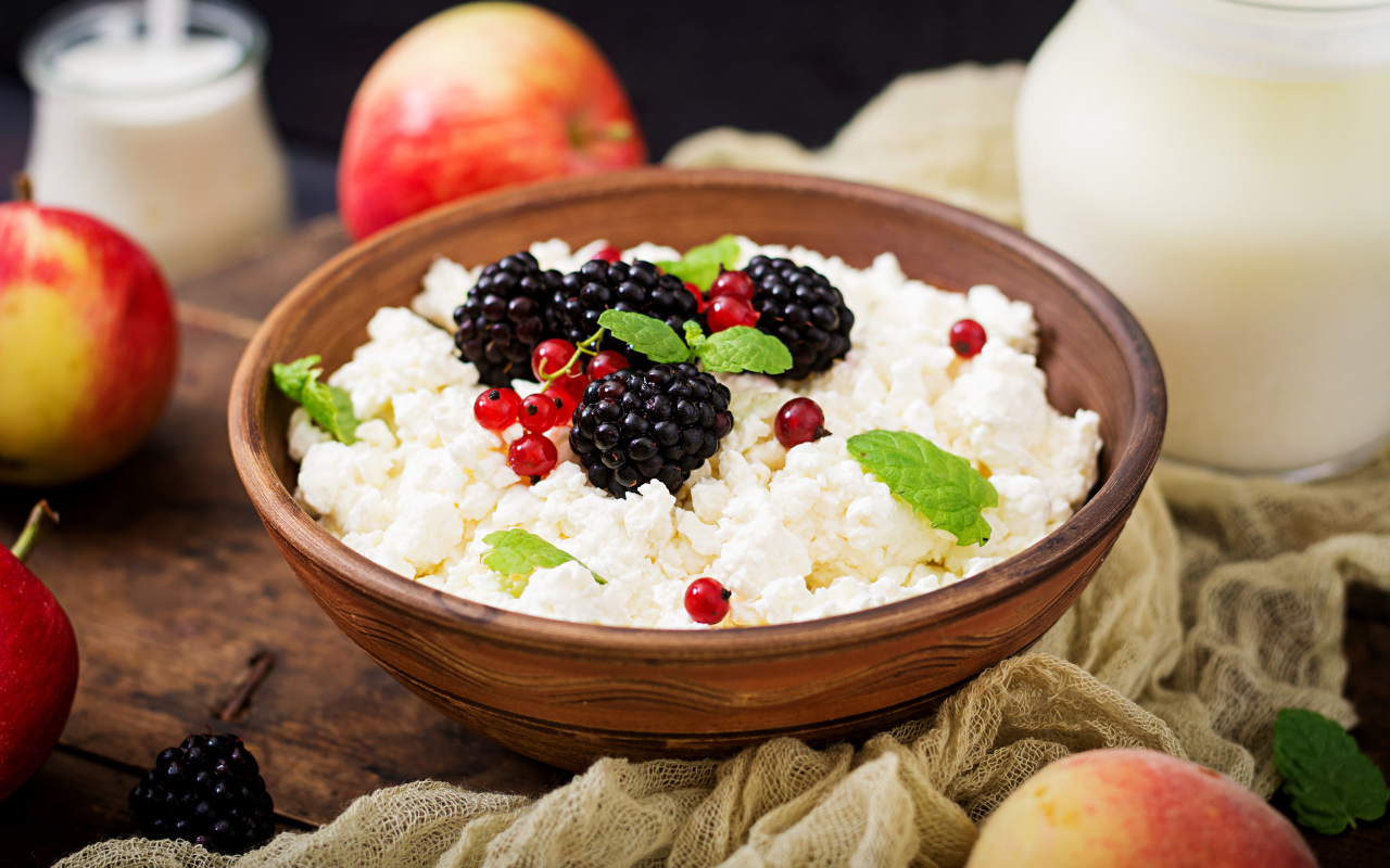 Творог с ягодами в деревянной миске на столе с яблоками