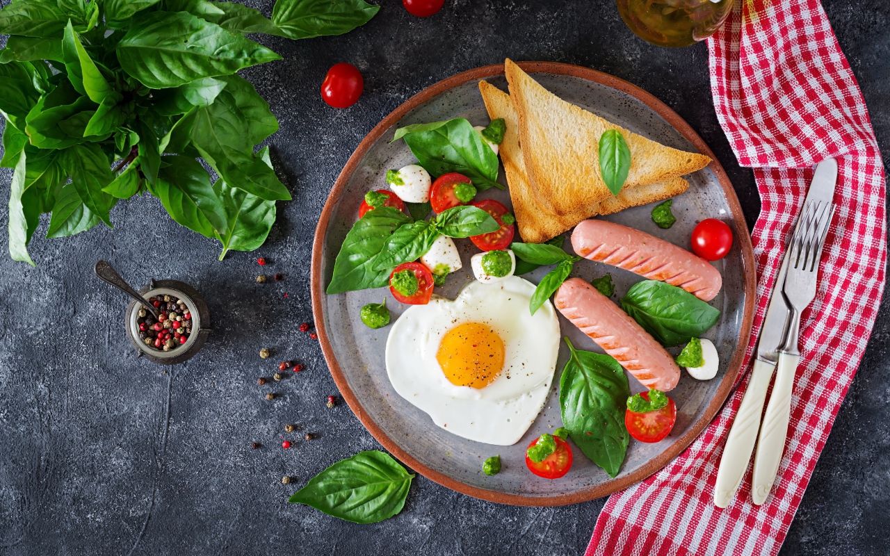 Яичница на тарелке с помидорами, гренками, сыром, сосисками и зеленью базилика