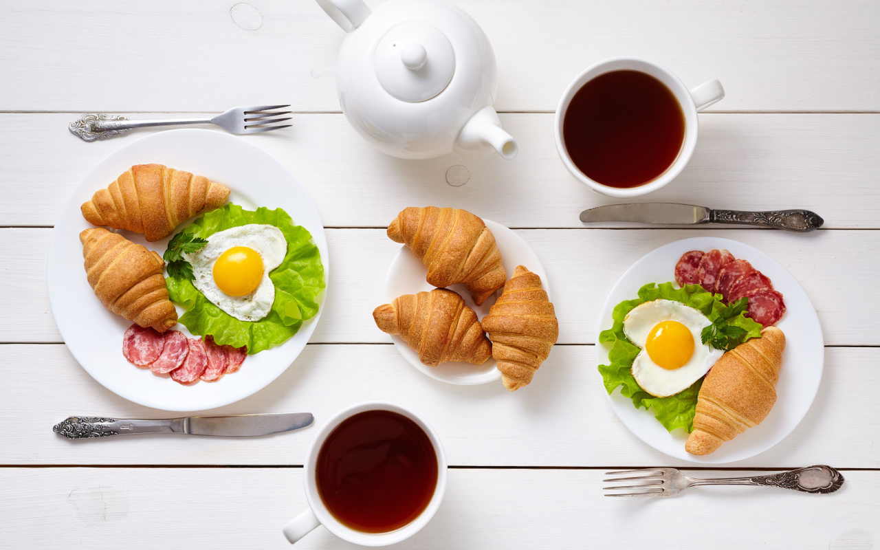 Яичница с колбасой и круассанами на столе чаем 