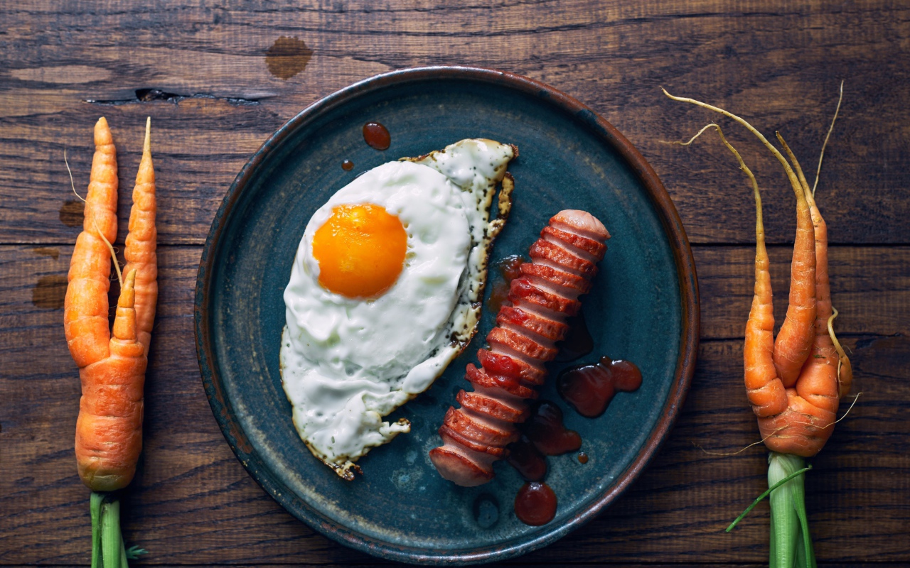 Яичница с сосиской на столе с морковью 