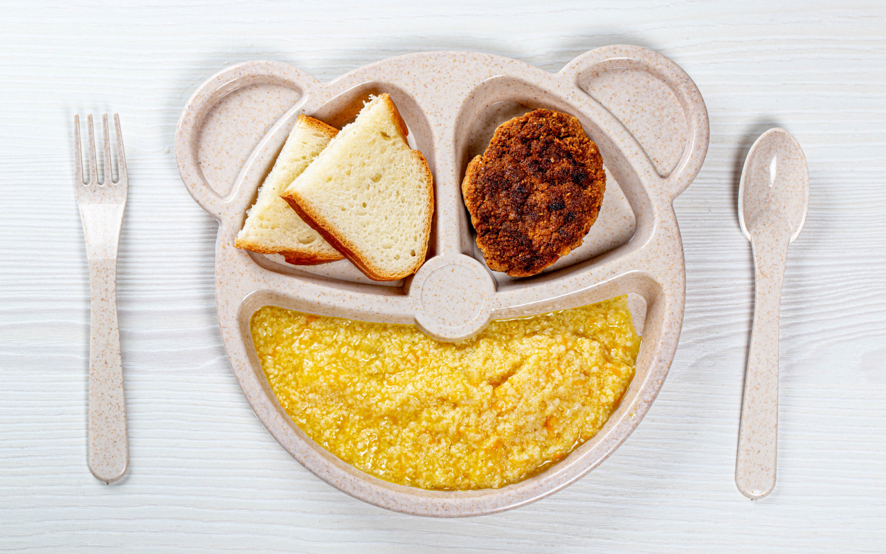 Каша на тарелке с котлетой и хлебом для ребенка