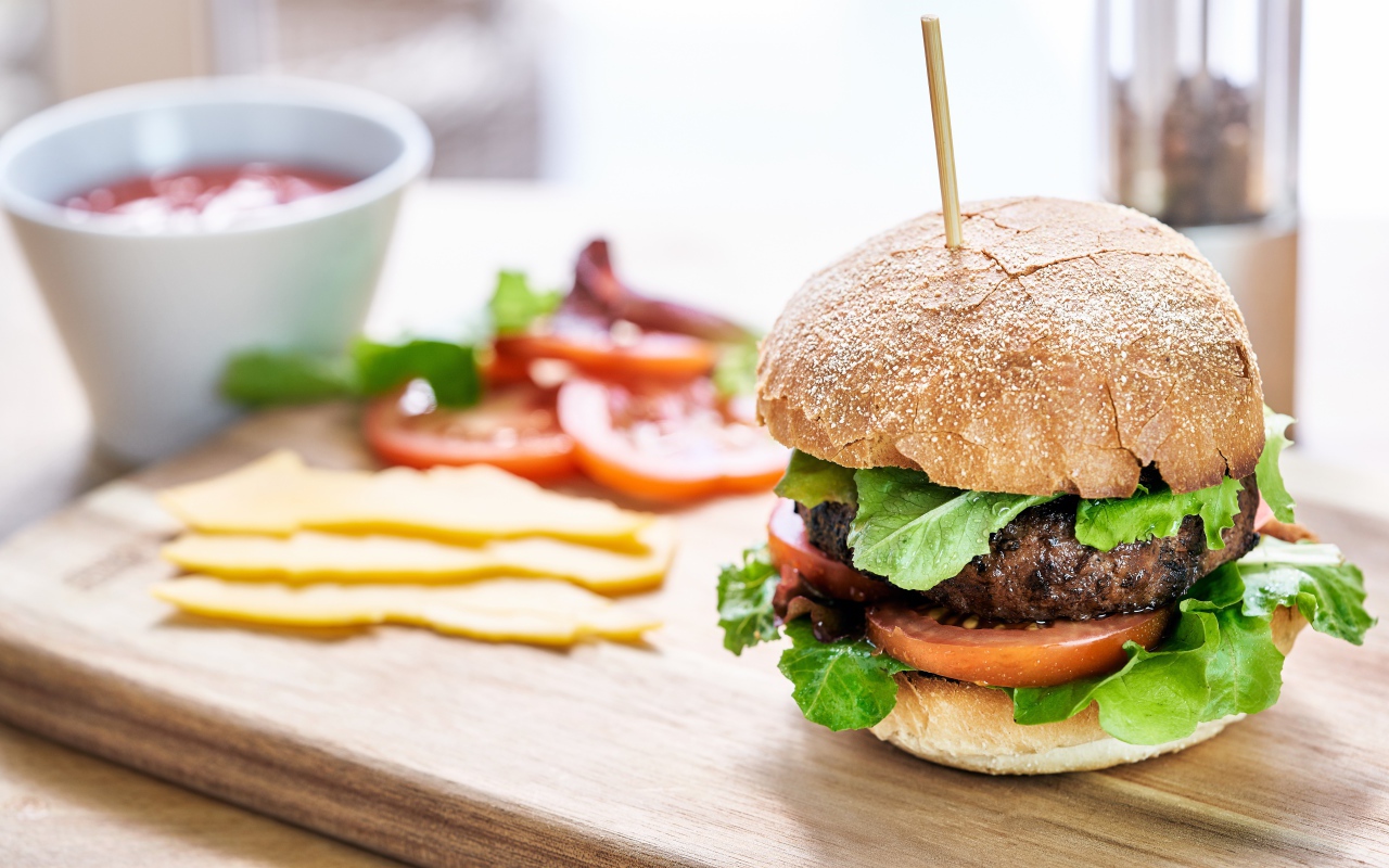 Аппетитный гамбургер на доске с сыром и помидорами