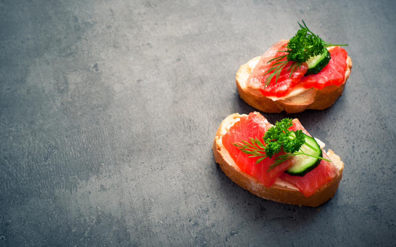 Два бутерброда с красной рыбой, огурцом и зеленью на черном фоне