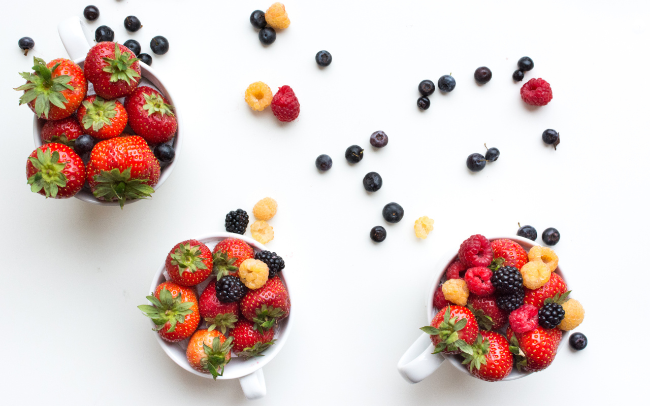 Чашки на столе с ягодами клубники, малины и ежевики 