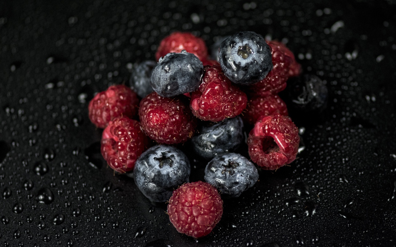 Мокрые ягоды черники и малины на черном фоне