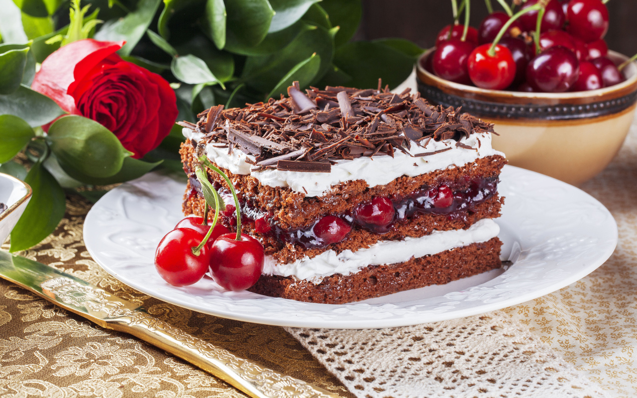 Кусок торта с вишней, шоколадной крошкой на столе с розой