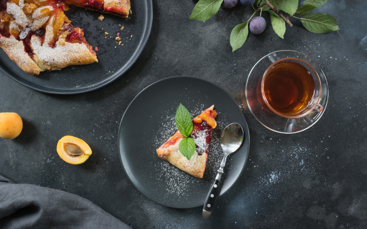 Кусок пирога с сахарной пудрой и абрикосами и сливами на столе с чаем 