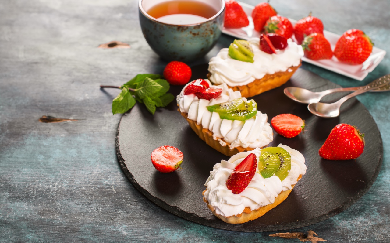 Пирожные с киви и клубникой на столе с чаем