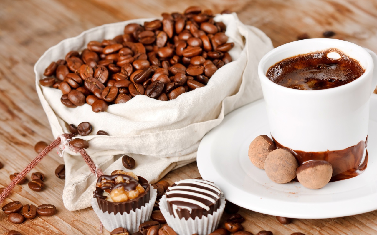 Шоколадные конфеты на столе с чашкой кофе и мешком с кофейными зернами