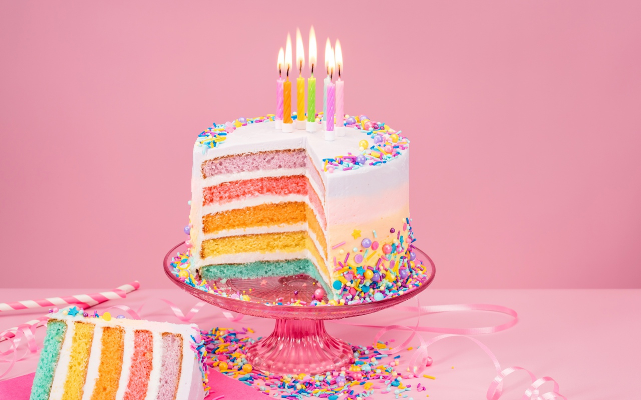 Разноцветный праздничный торт со свечами на розовом фоне