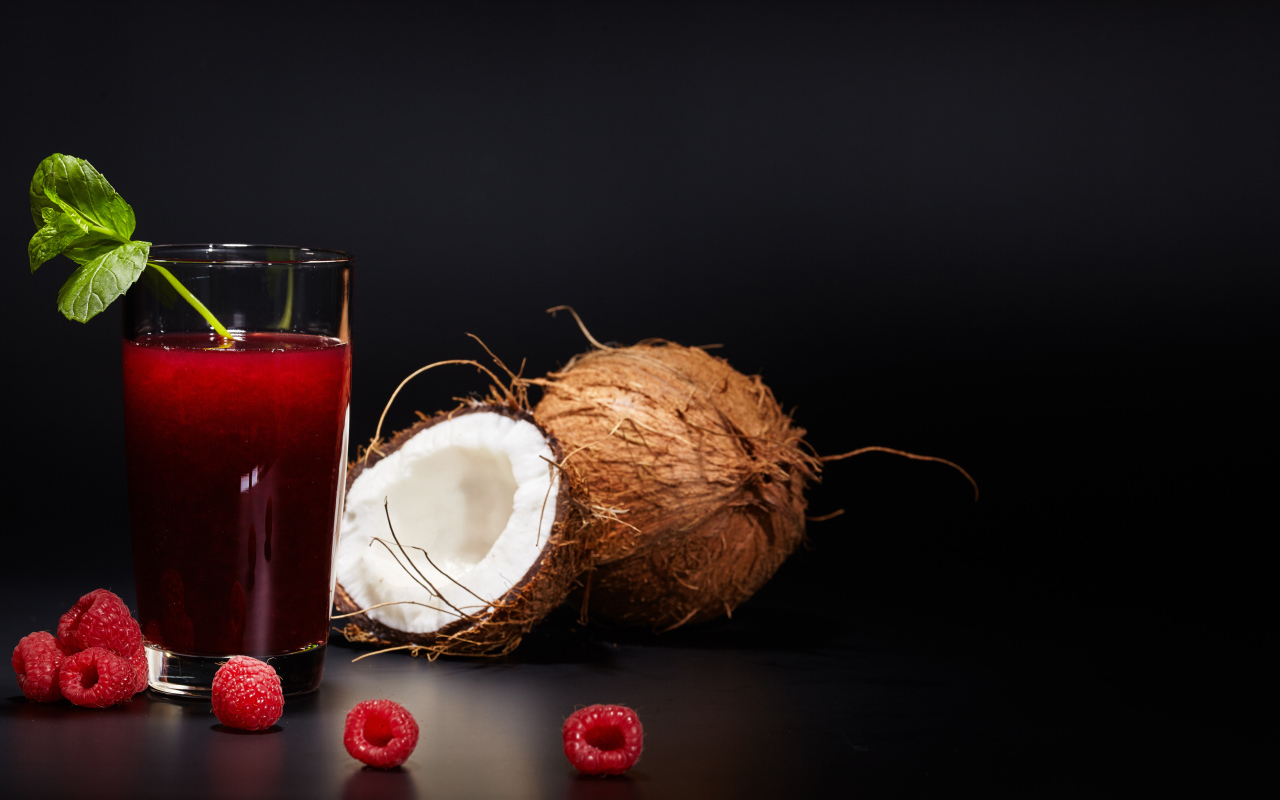 Стакан сока на столе с кокосом и ягодами малины 