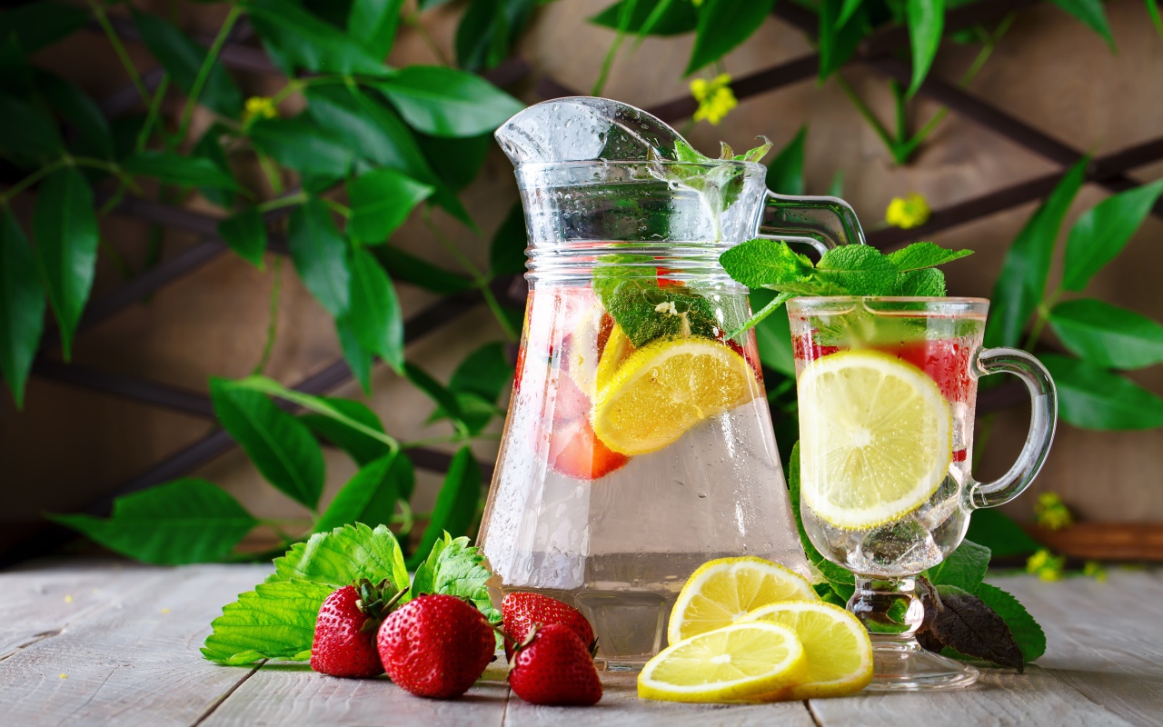 Холодный мохито в графине на столе с клубникой и лимоном