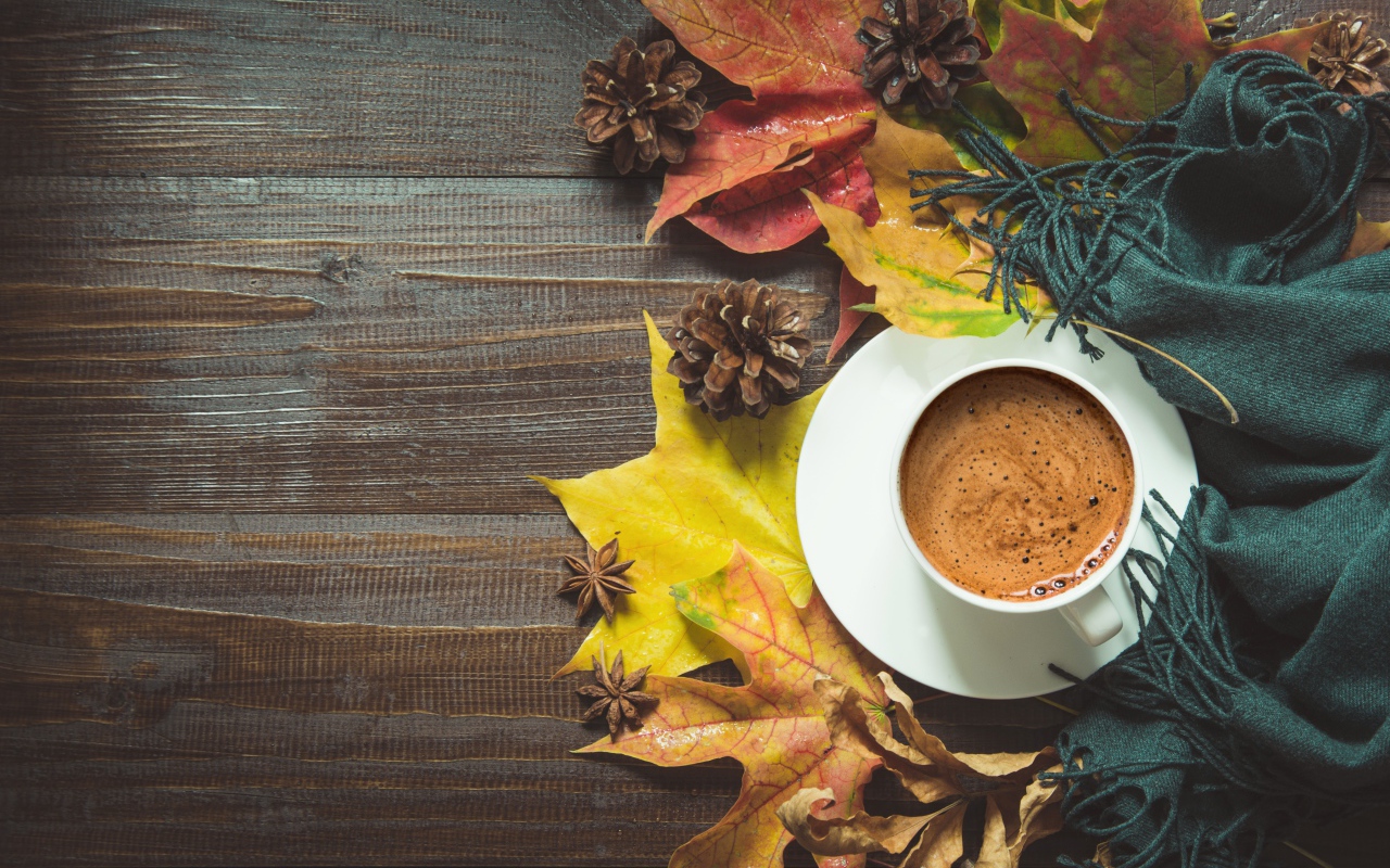 Чашка кофе на столе с шарфом, желтыми листьями и шишками