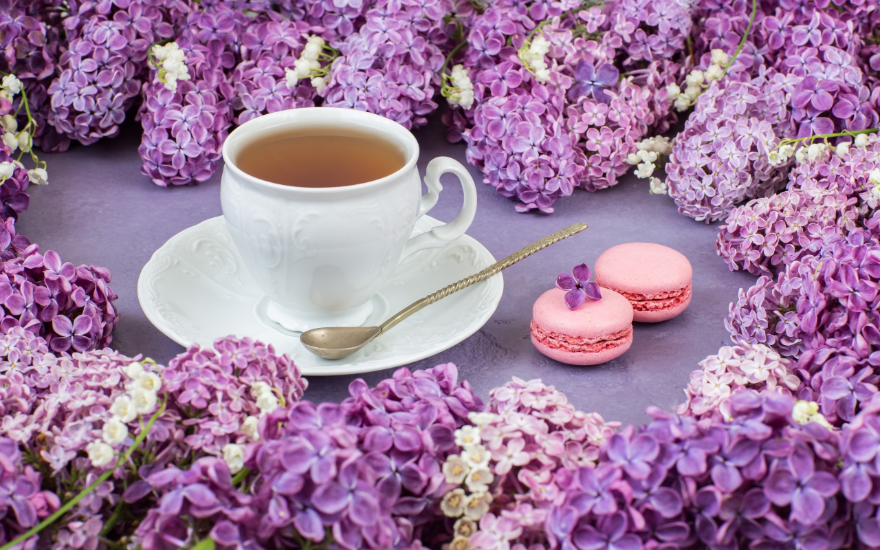 Чашка чая на столе с цветами сирени и десертом макарон
