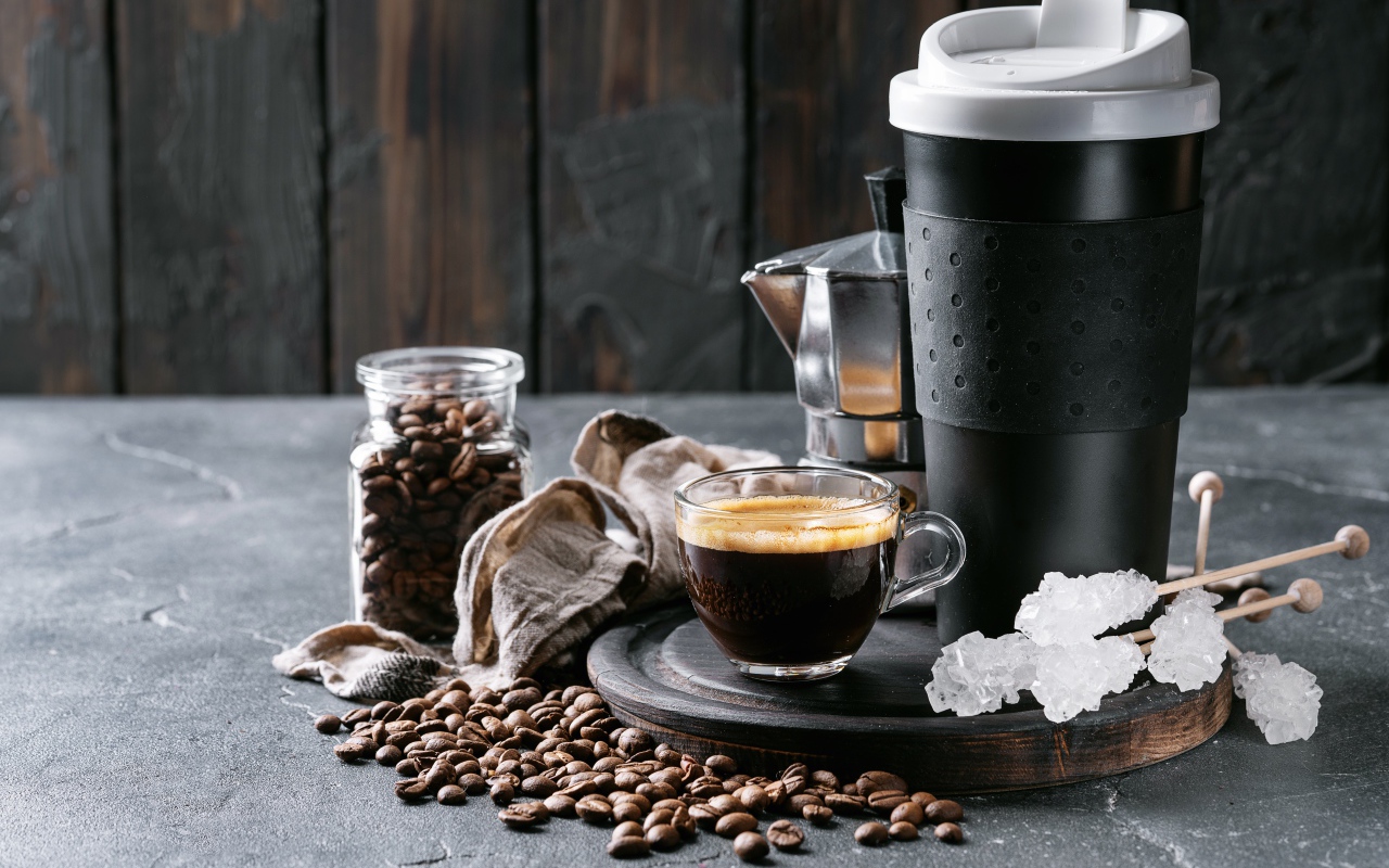 Стеклянная чашка кофе на столе с термосом и зернами