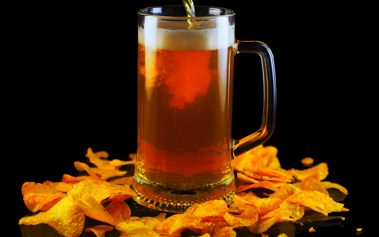 Бокал пива с чипсами на черном фоне