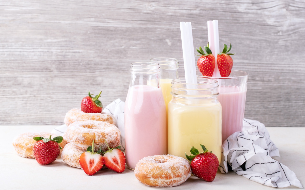 Молочные коктейли на столе с пончиками и ягодами клубники 