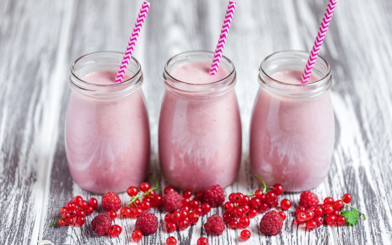 Три банки ягодного  смузи на столе с ягодами малины и смородины