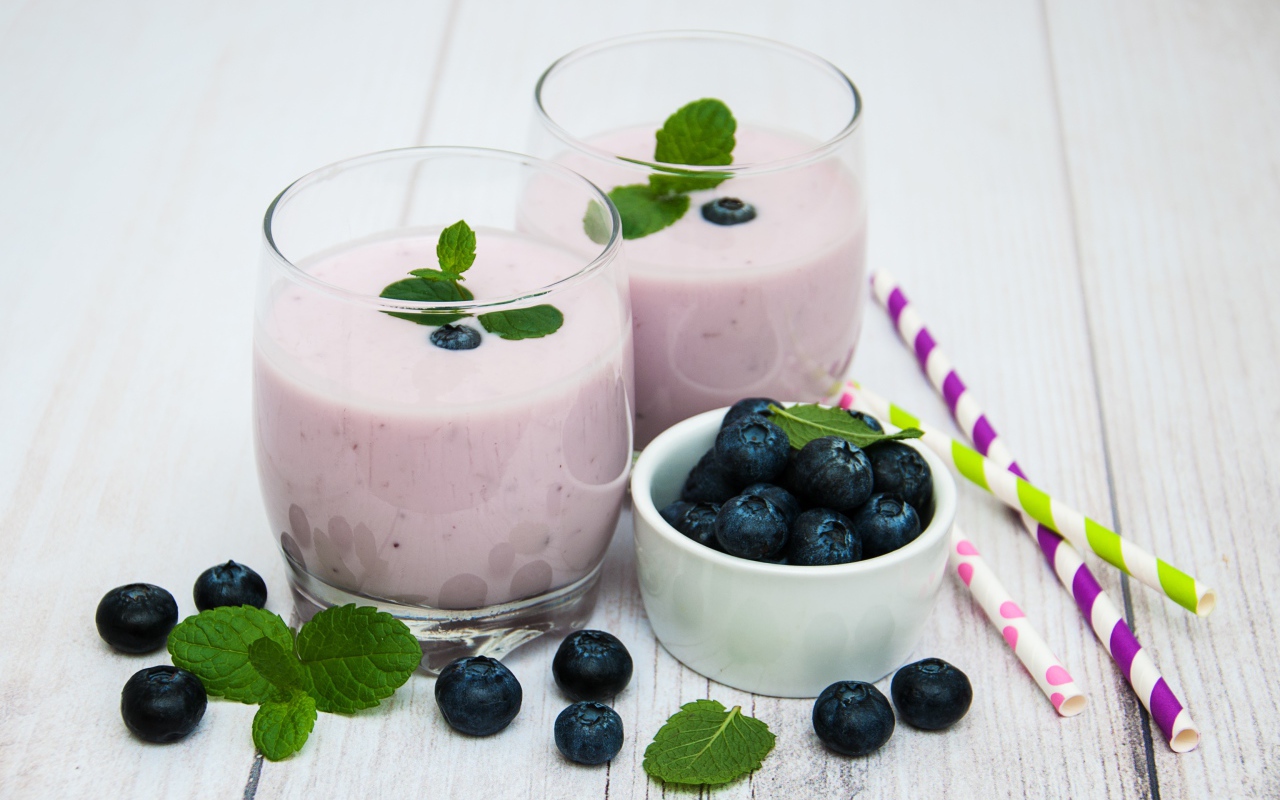 Два стакана коктейля в стаканах на столе с ягодами черники и трубочками