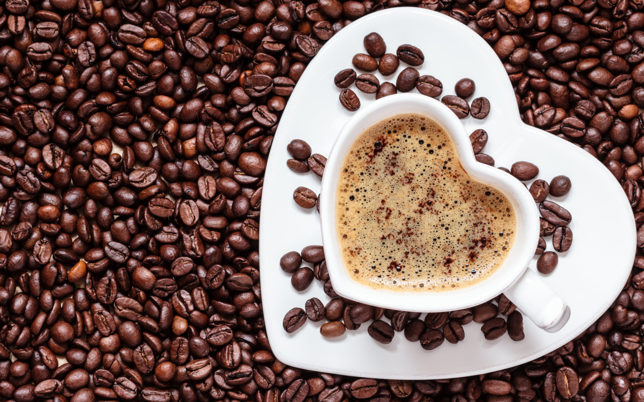 Белая чашка в форме сердца стоит на кофейных зернах 