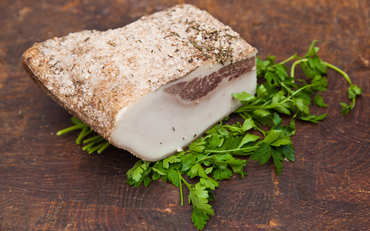 Кусок сала со специями на столе с зеленью петрушки