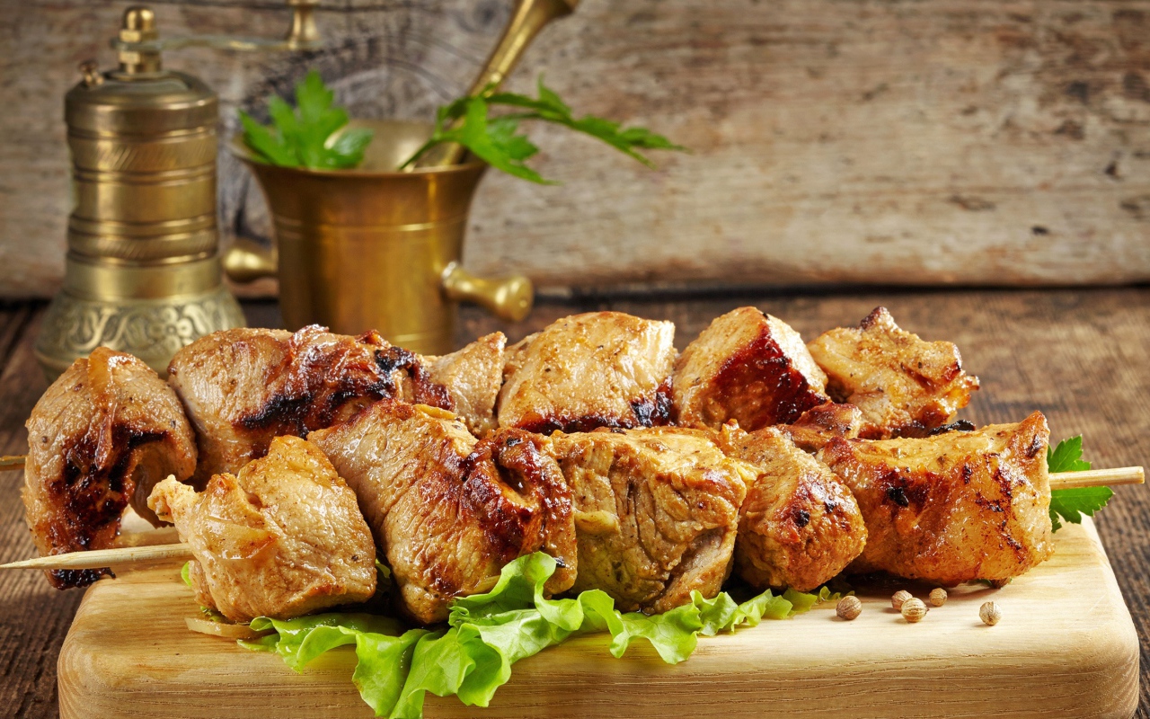 Аппетитный шашлык лежит на разделочной доске с листьями салата