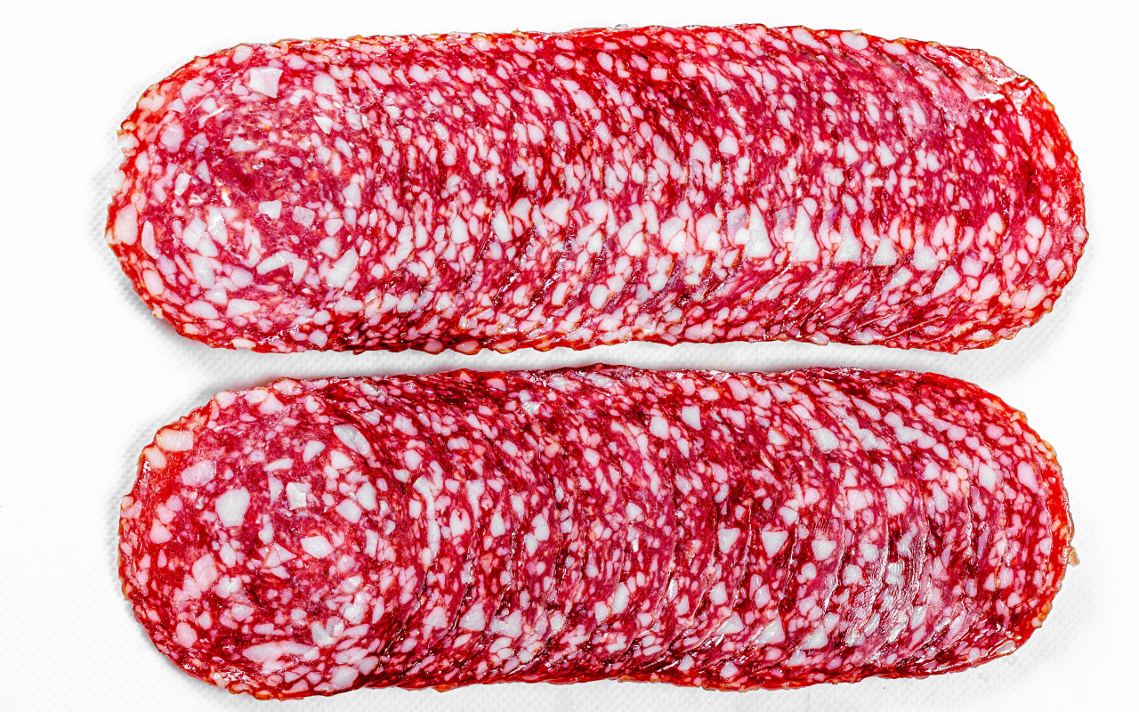 Колбаса салями нарезанная тонкими кусочками на белом фоне