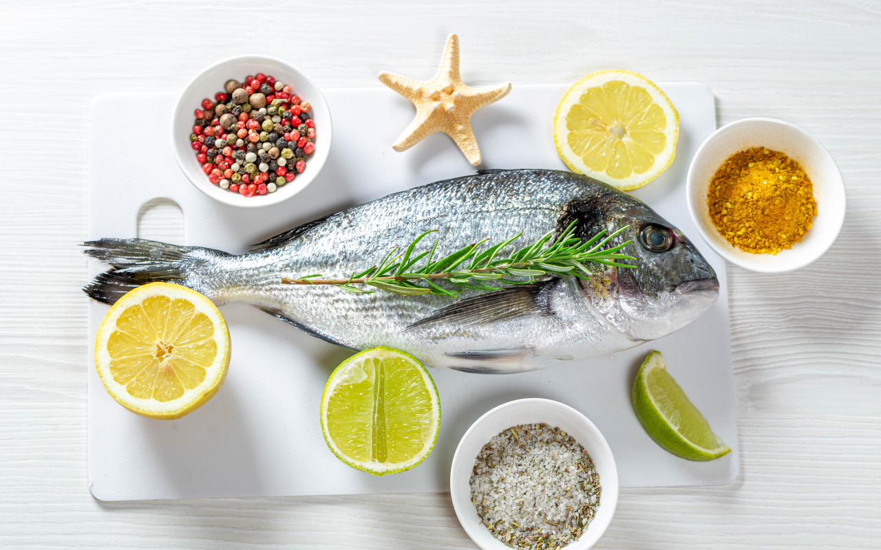 Свежая рыба на доске с солью, перцем, куркумой и лимоном