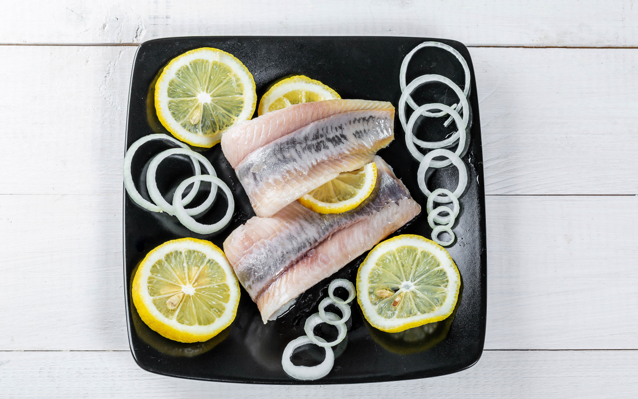 Herring fillet on a black plate with onions and lemon