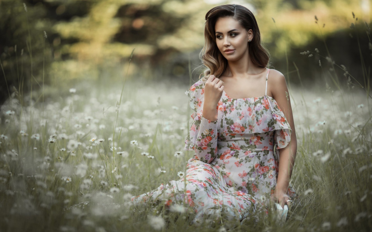 Красивая девушка в сарафане сидит на поляне с ромашками 