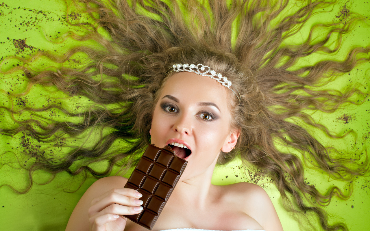 Красивая девушка с украшением в волосах лежит с шоколадкой 
