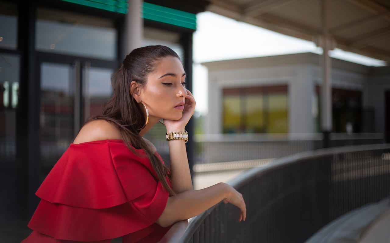 Задуманная девушка в красном платье стоит у перил 