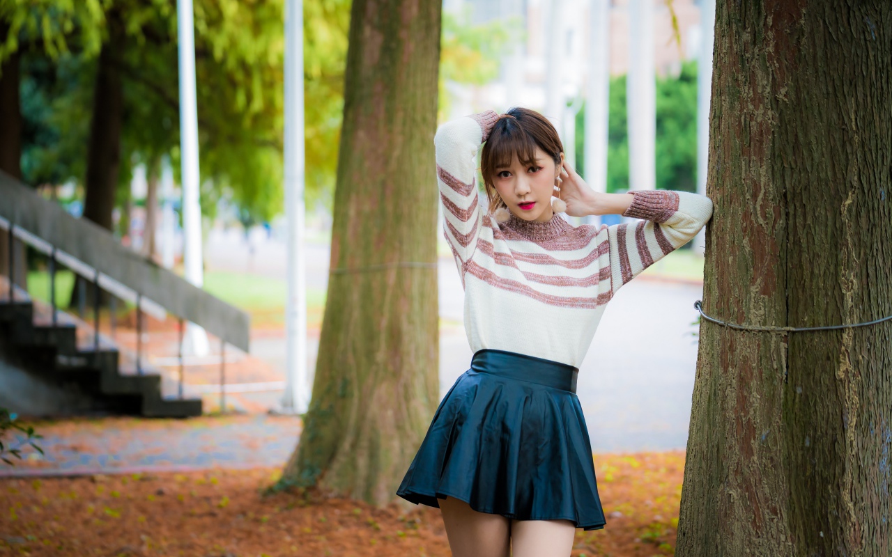 Девушка азиатка стоит в короткой юбке у дерева