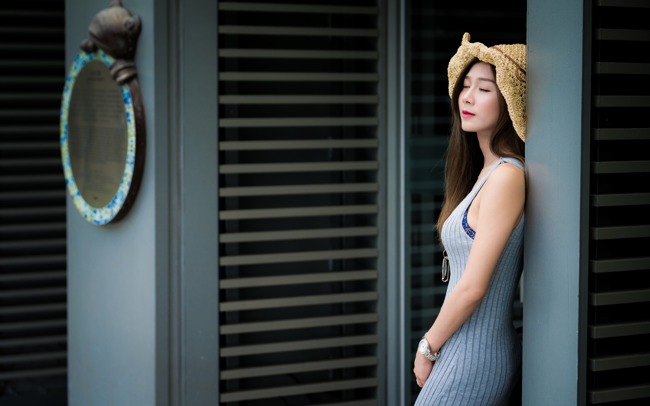 Девушка азиатка с закрытыми глазами стоит у стены 