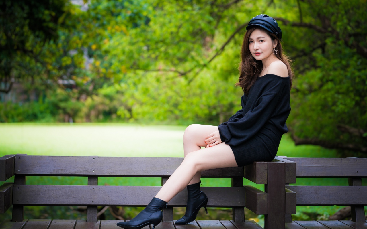 Красивая девушка азиатка в черном платье сидит на деревянной лавке