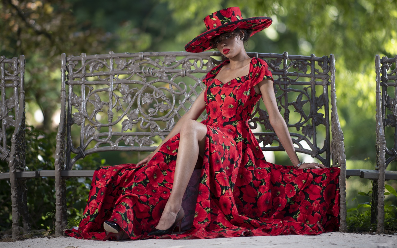 Красивая темнокожая девушка в красном платье сидит на лавке