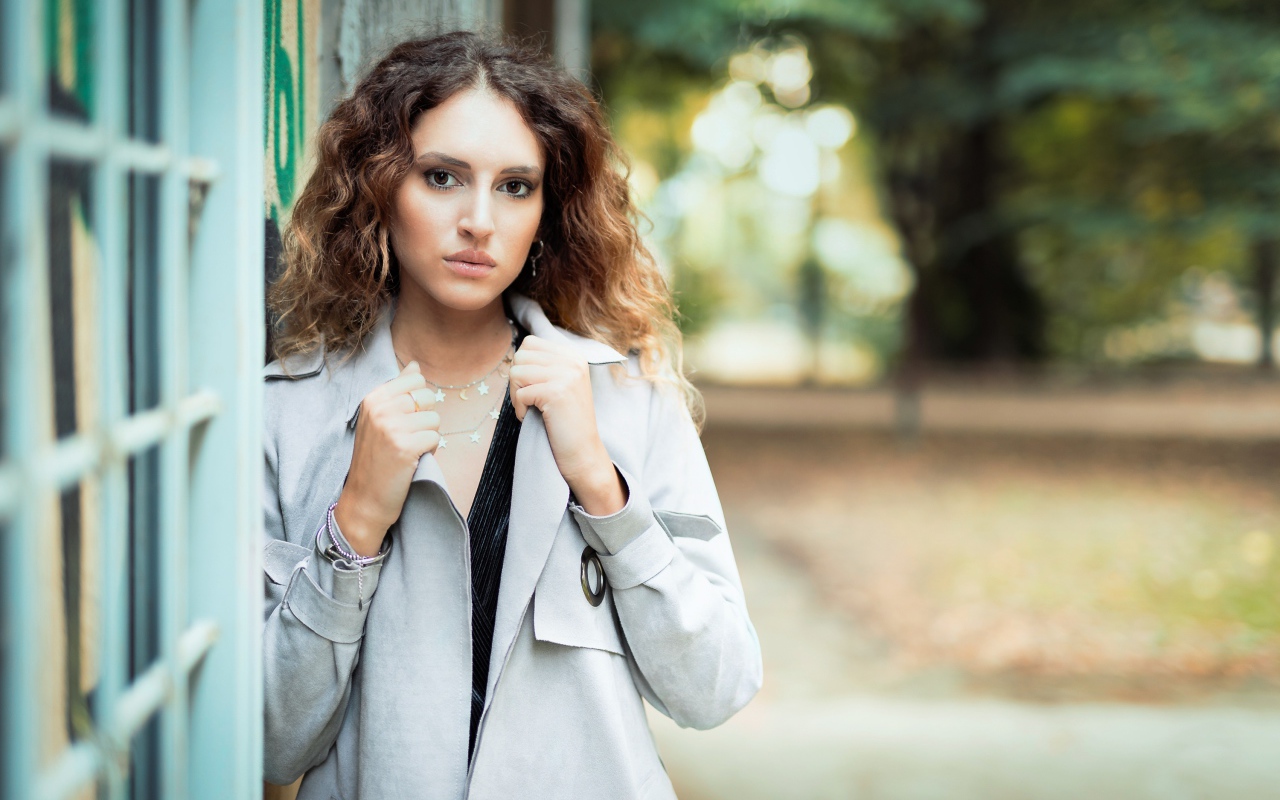 Красивая девушка в сером плаще у стены