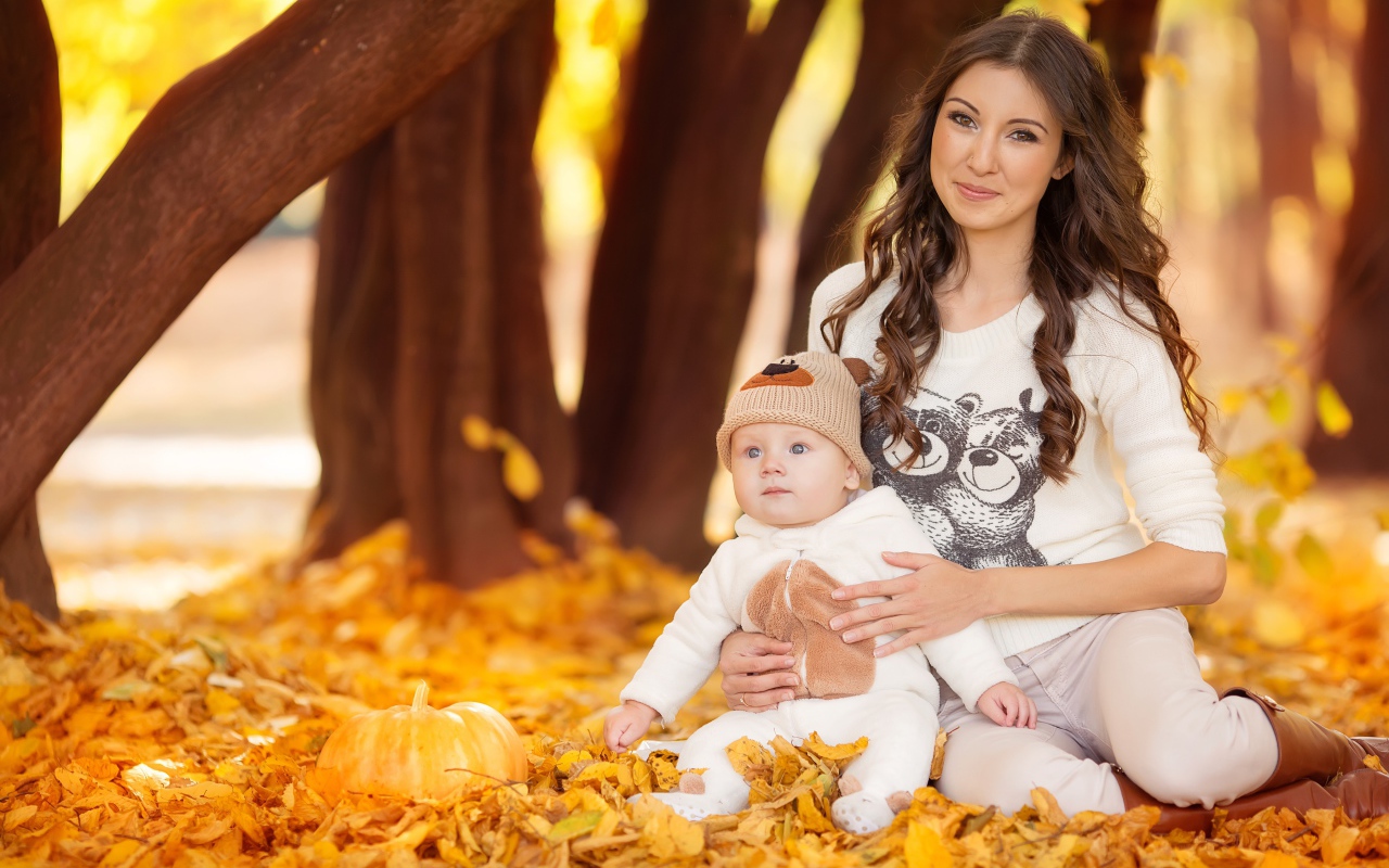 Красивая девушка сидит с грудным ребенком на опавшей листве