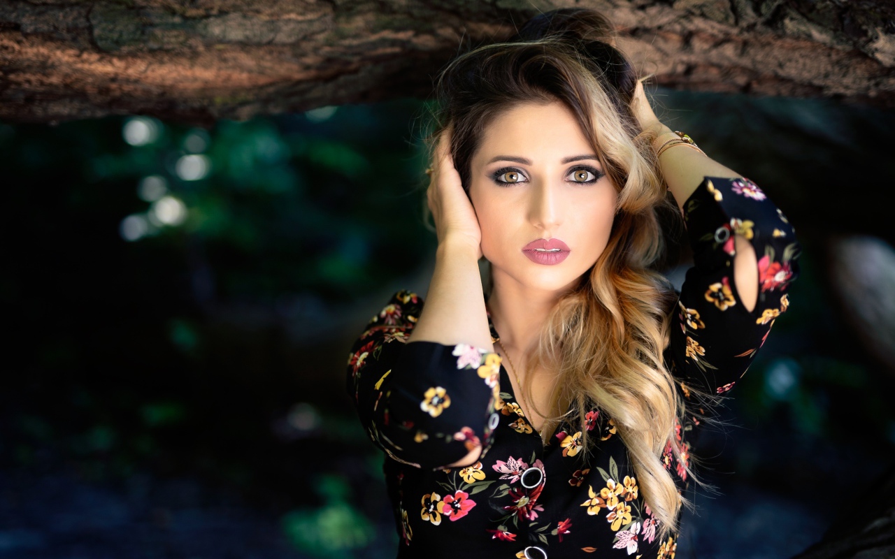 Красивая девушка с руками в волосах у дерева