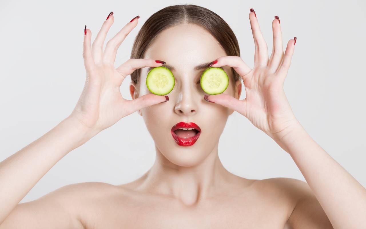 Яркая девушка с огурцами у глаз на сером фоне