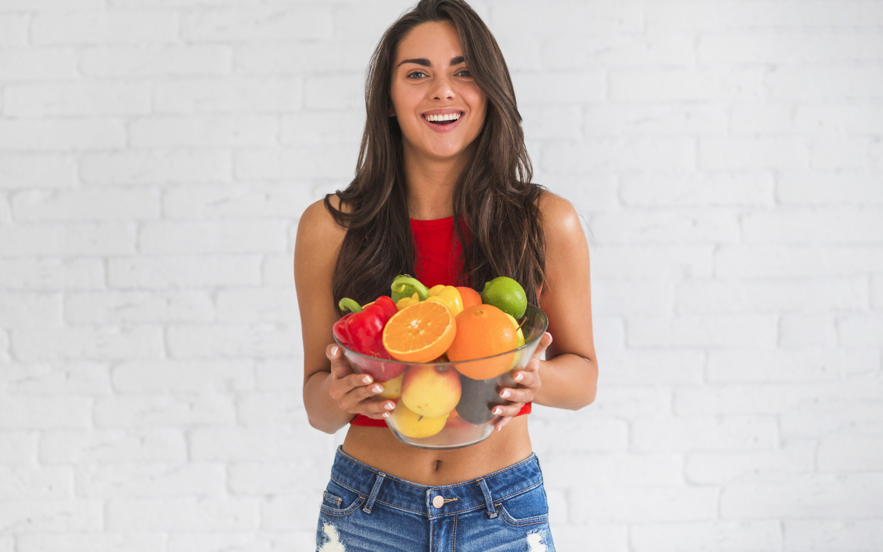 Брюнетка с миской фруктов на фоне стены