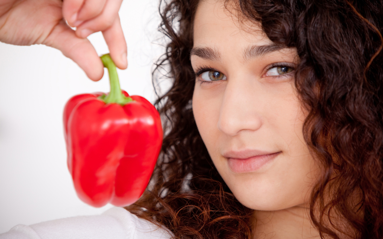 Лицо девушки с красным сладким перцем в руке крупным планом
